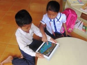 Two young Cambodian children play an educational game on a tablet.